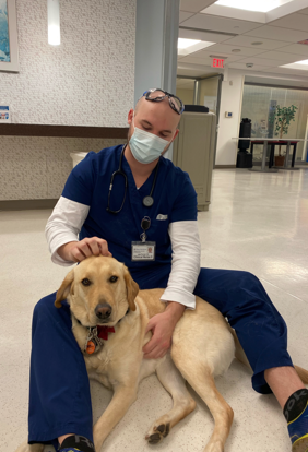 Jake Purnell sits on the hospital floor petting a dog